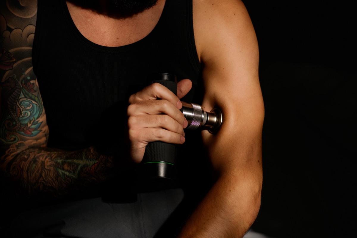 A man using the Spalux Pulse massage gun on his upper arm